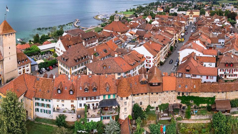 A historic town with a prominent tower, red-roofed buildings, and a waterfront.