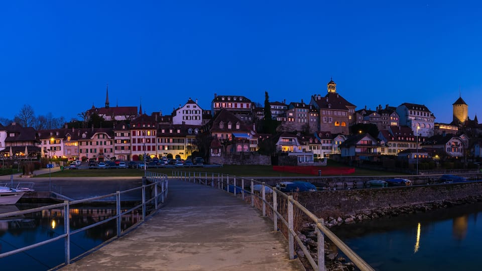 A waterfront town at dusk with a prominent tower and a boat docked at the pier.