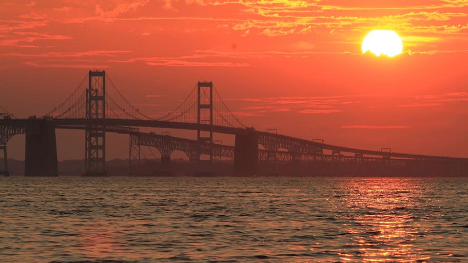A bridge silhouetted against a sunset with the sun visible near the horizon.
