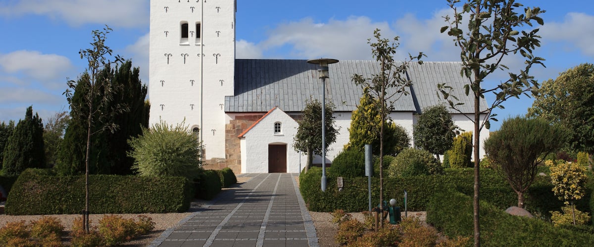 A church with a tall tower and a brick pathway leading to the entrance.