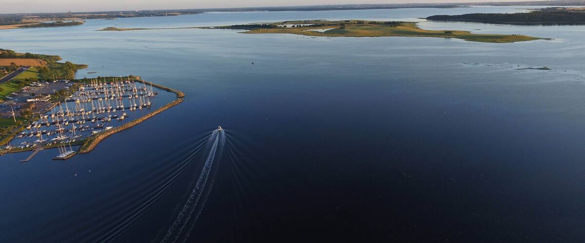 An aerial view of a marina surrounded by calm waters, with a clear sky and distant landforms.