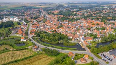 An aerial view of a town with red-roofed houses, a river, and surrounding greenery.