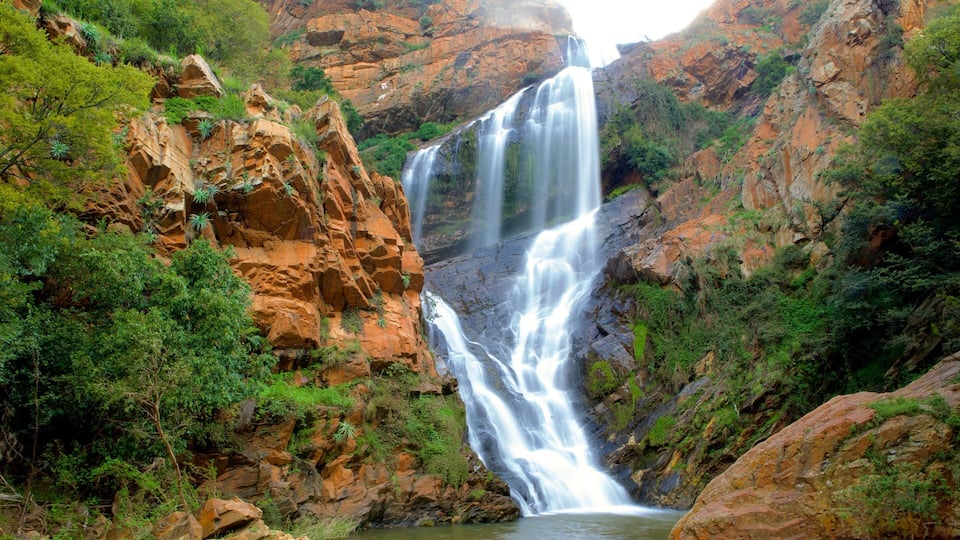 Une cascade à plusieurs niveaux, entourée de falaises rocheuses et d’une végétation luxuriante.