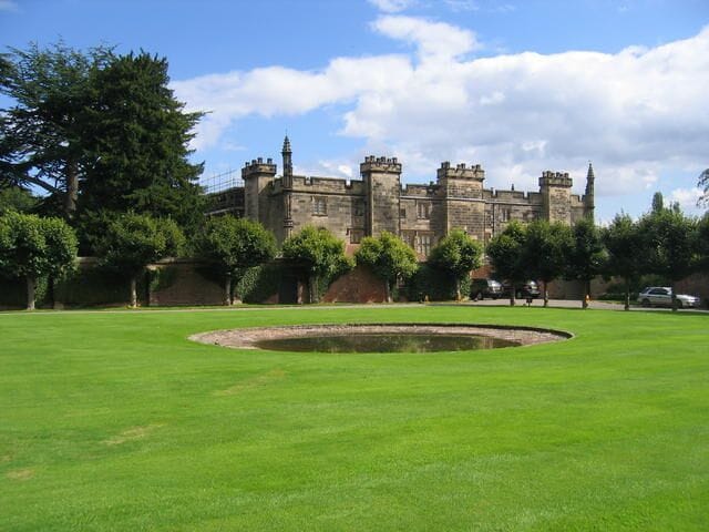 Un grand château doté d’une pelouse circulaire et d’un étang à l’avant.