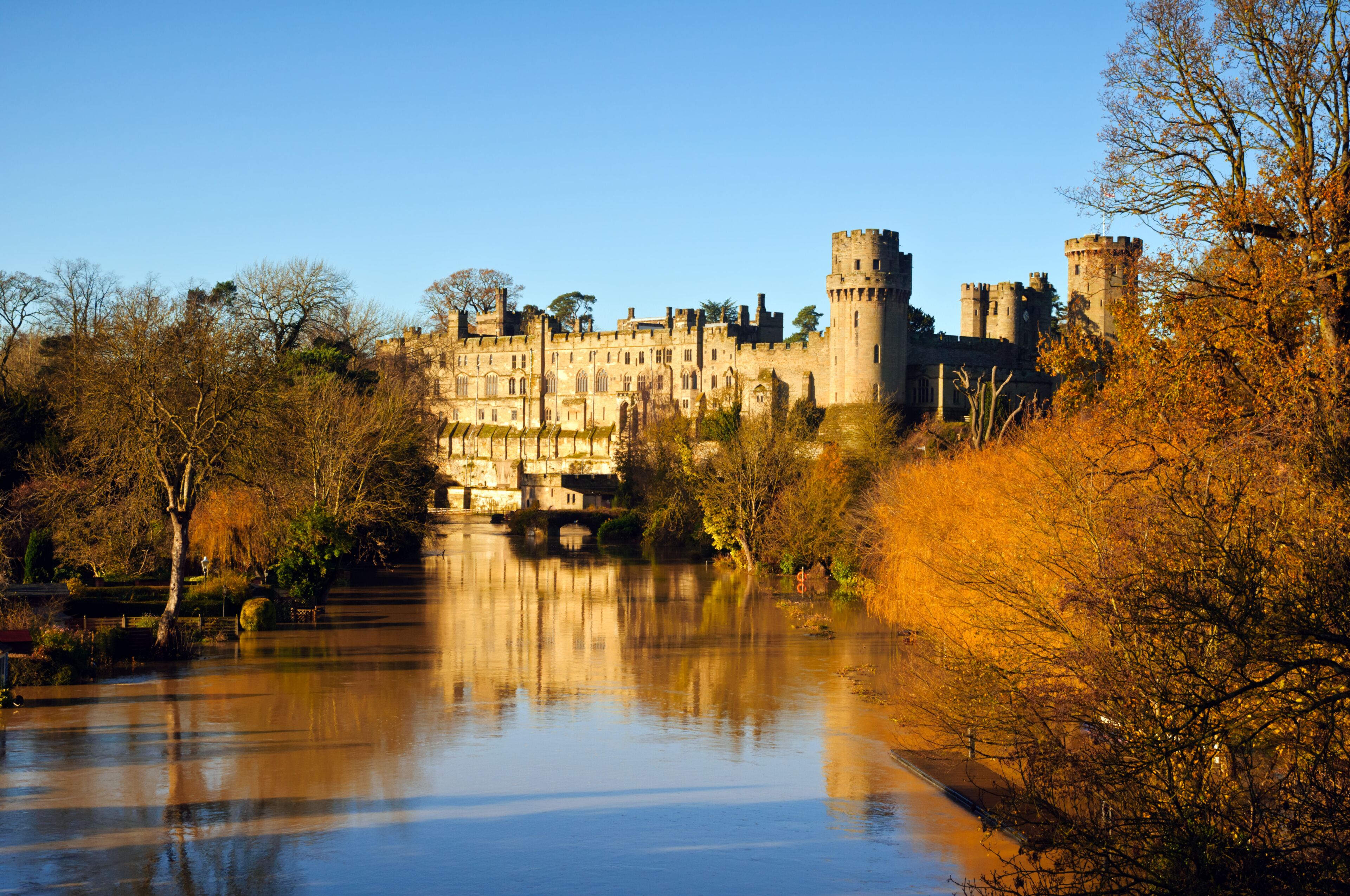 A historic castle with towers, a moat, and autumn trees.