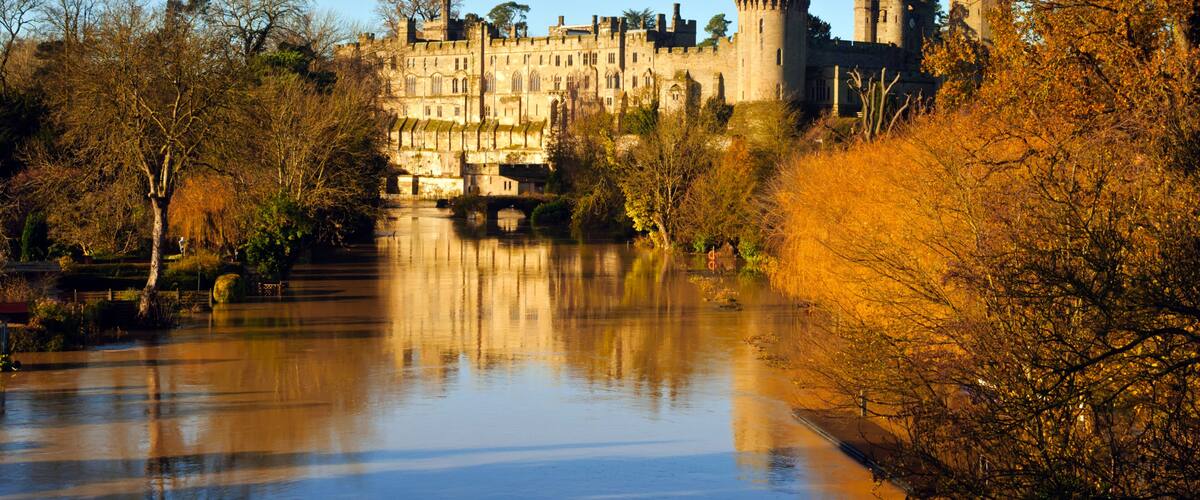 A historic castle with towers, a moat, and autumn trees.