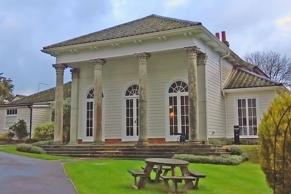A stately white building with columns and arched windows, a front porch, and a picnic table in the foreground.