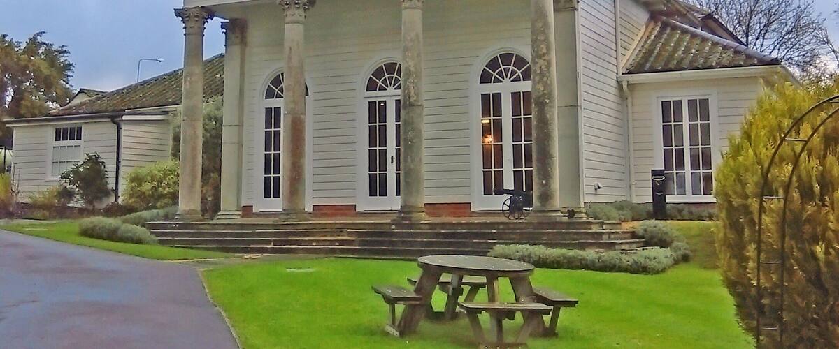 A stately white building with columns and arched windows, a front porch, and a picnic table in the foreground.