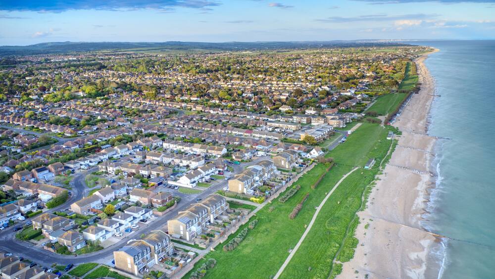 An aerial view of a coastal residential area with houses, a beach, and a clear sky.