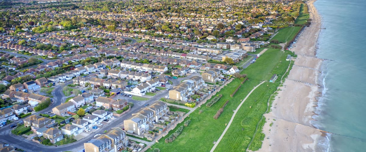 An aerial view of a coastal residential area with houses, a beach, and a clear sky.