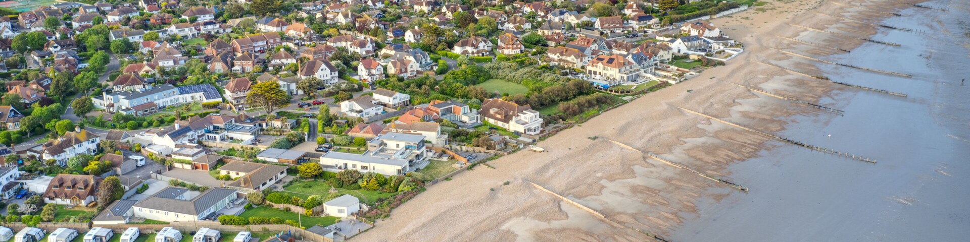 Vista aérea de un pueblo costero con casas, una playa y un paisaje verde al fondo.