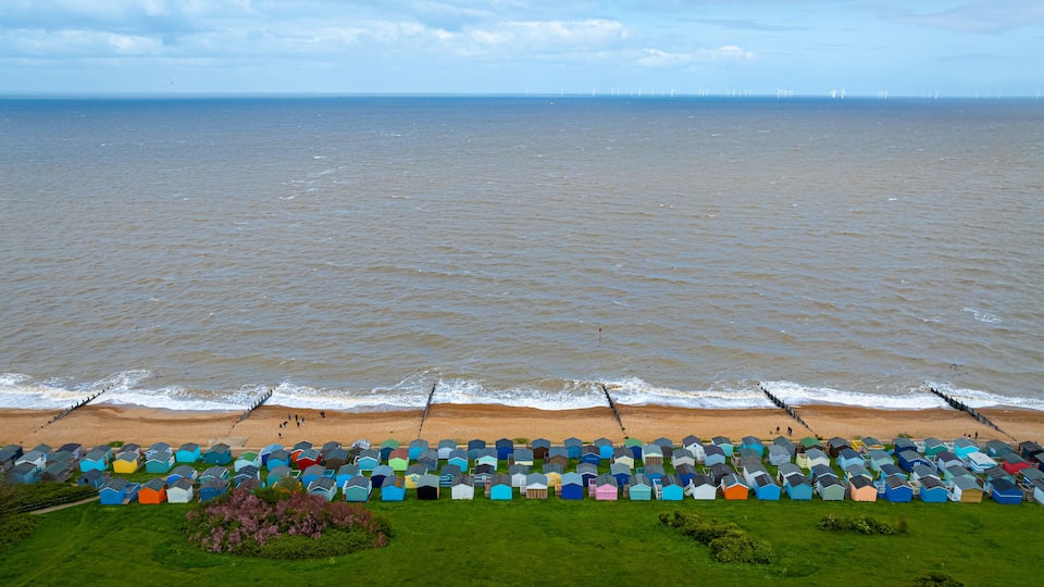 A beach with colorful beach huts and wind turbines in the distance.
