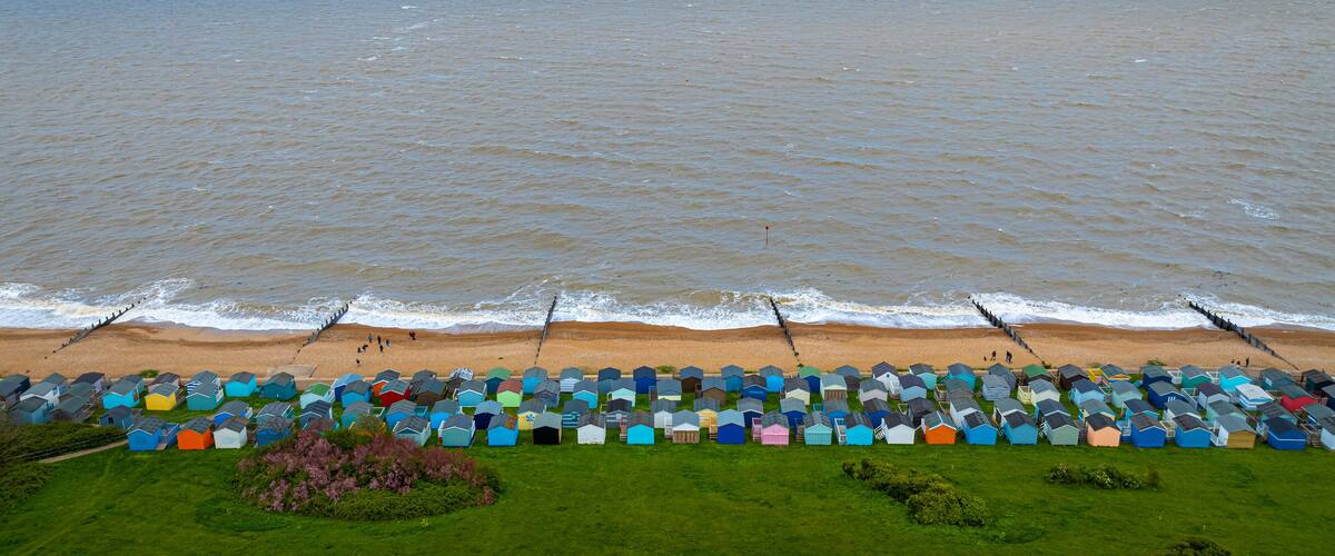 A beach with colorful beach huts and wind turbines in the distance.