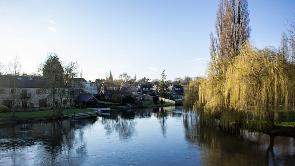 A calm river reflecting buildings and trees.