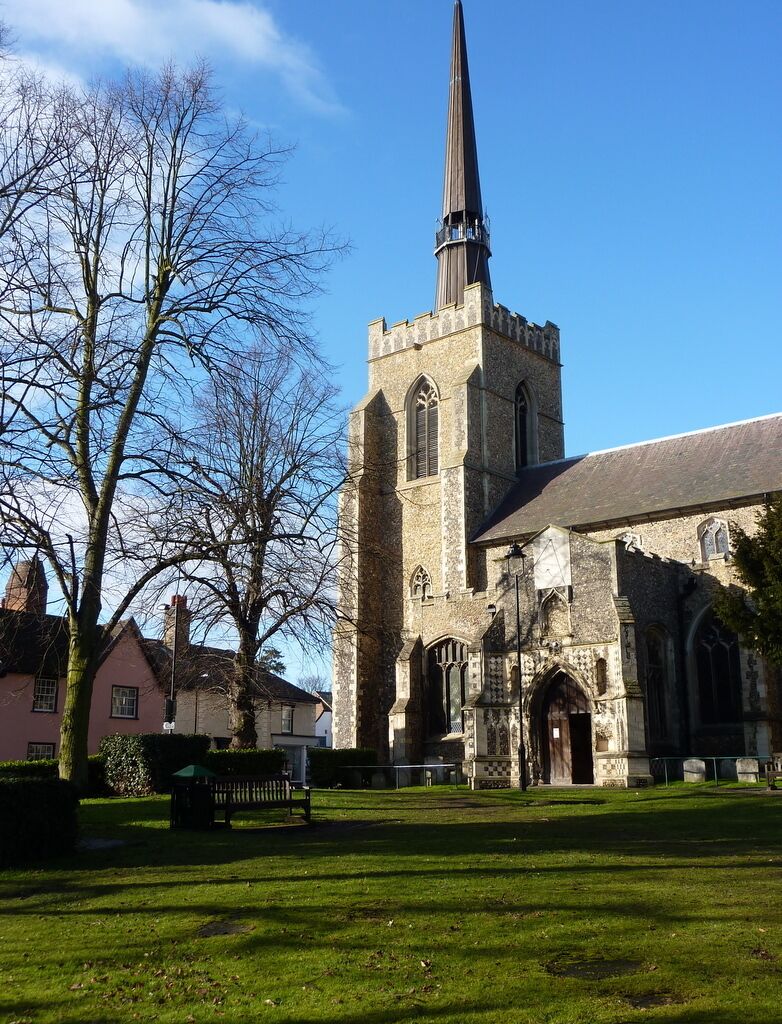 A church with a tall spire, a stone tower, and a grassy courtyard with a bench.