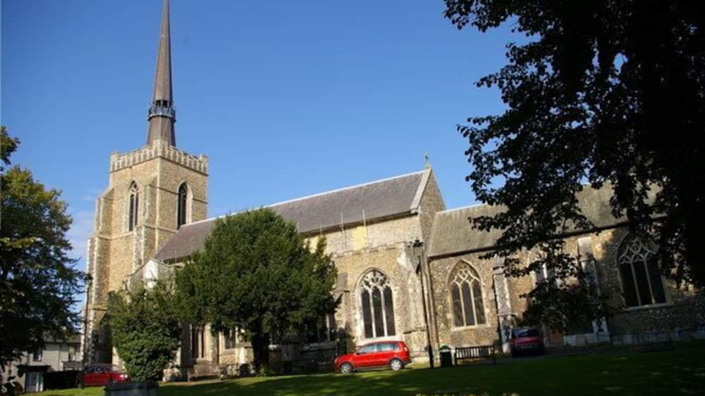 Une église dotée d’un clocher imposant, entourée d’arbres et d’une pelouse bien entretenue.
