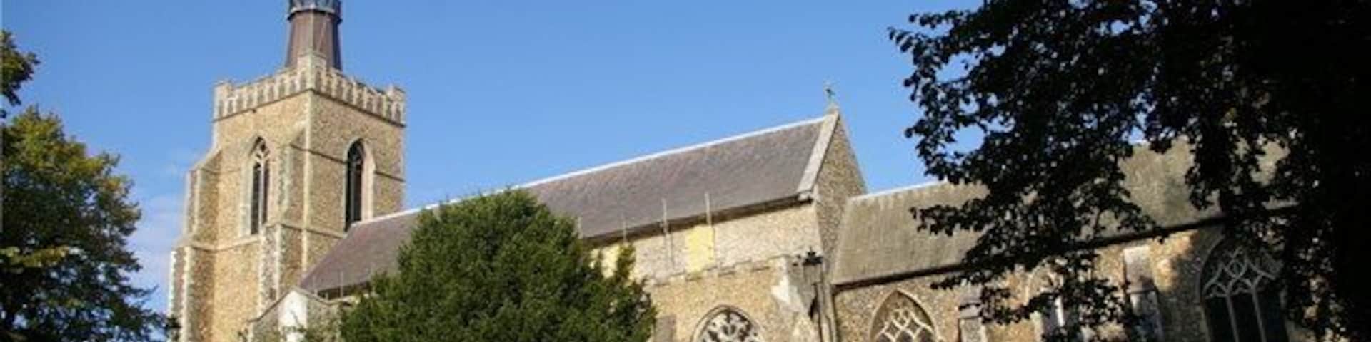 Una iglesia con un campanario alto, rodeada de árboles y un césped cuidado.