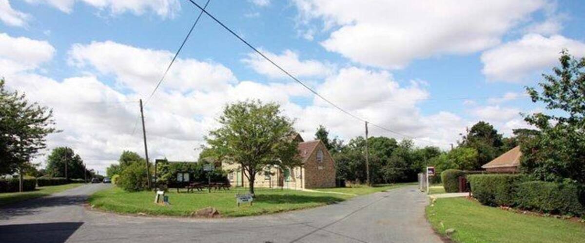 A quiet suburban street with houses, a grassy area, and a clear sky.