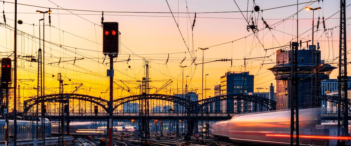Fast trains leaving and arriving at Munich main station (Germany) in warm evening light. Blurred light traces. Railway infrastructure, signals, glistening tracks, switches. Long exposure at sunset.