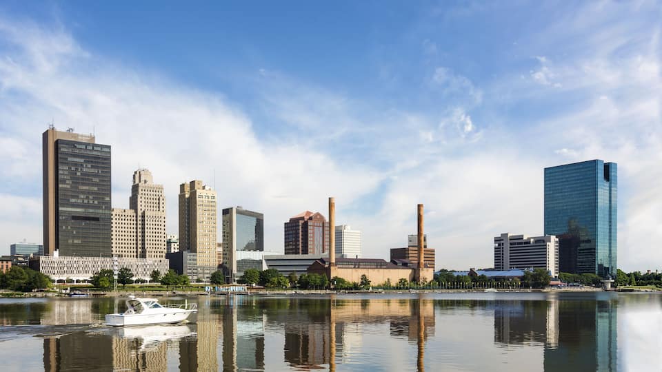 A city skyline with modern buildings and a river reflecting the structures.