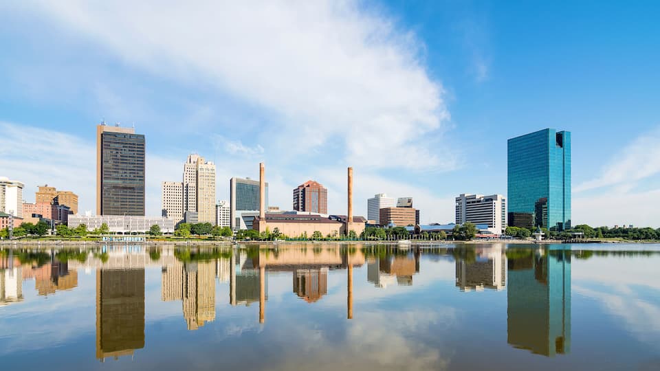 A city skyline with modern buildings and a calm lake reflecting the structures.