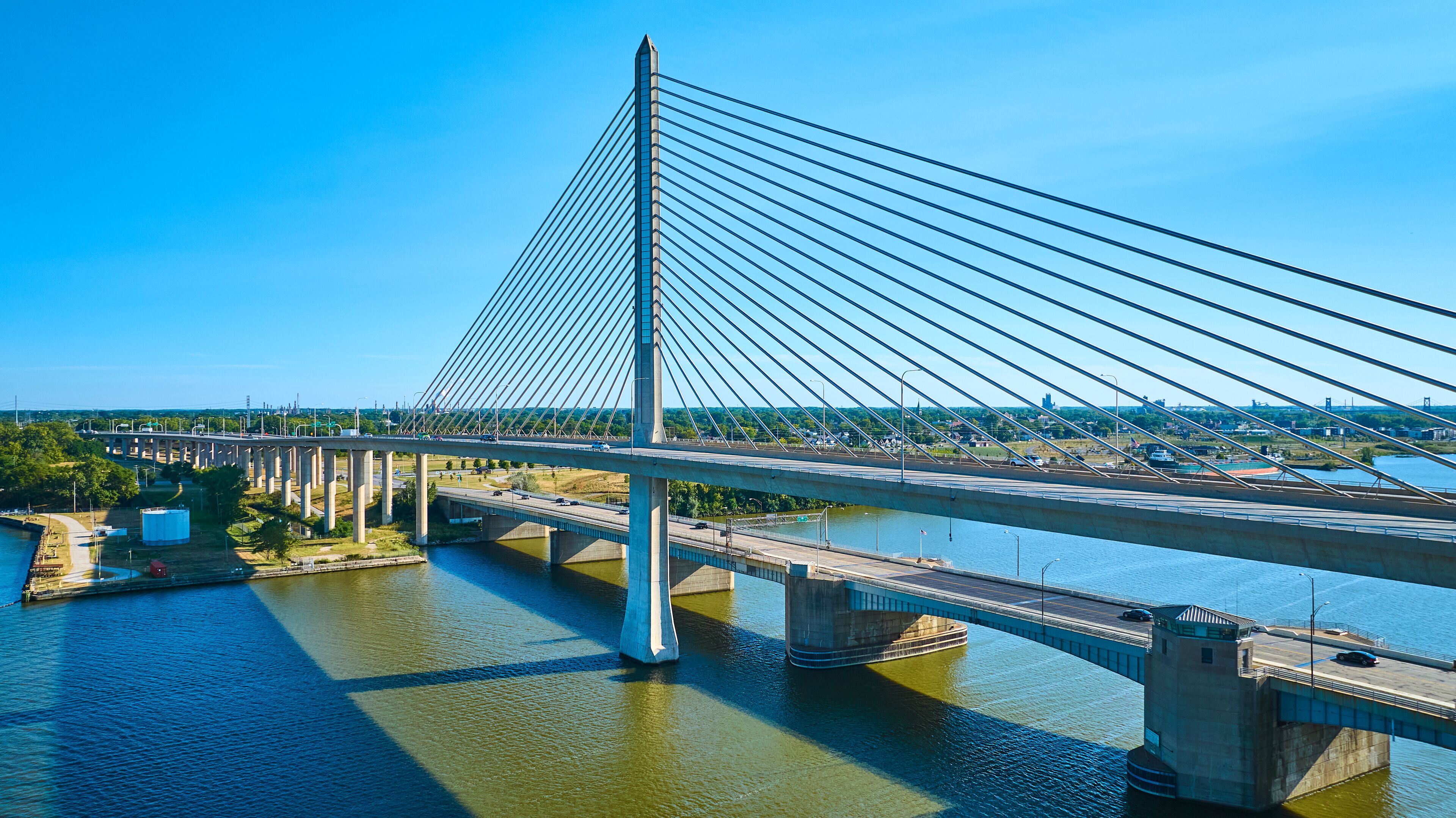 A cable-stayed bridge with multiple lanes, a river below, and a cityscape in the background.