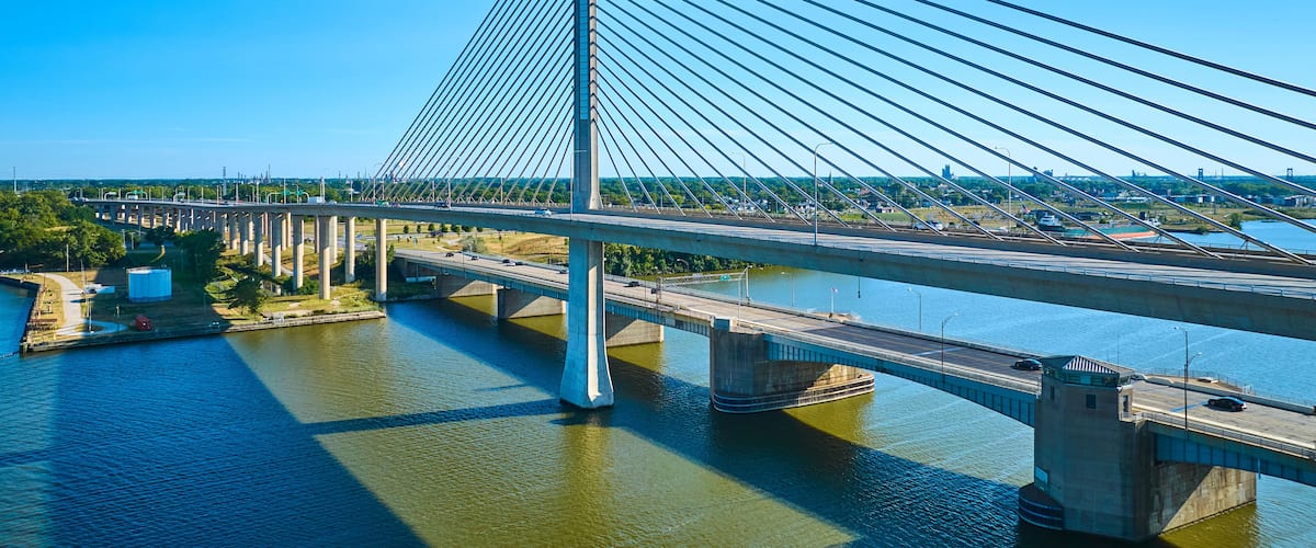 A cable-stayed bridge with multiple lanes, a river below, and a cityscape in the background.