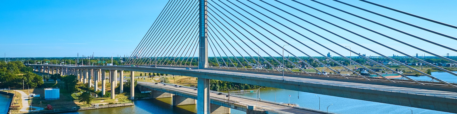 A cable-stayed bridge with multiple lanes, a river below, and a cityscape in the background.