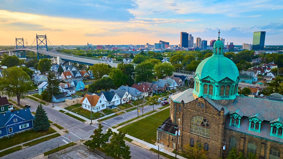 A cityscape with a prominent church with a turquoise dome, a large bridge, and modern buildings in the background.