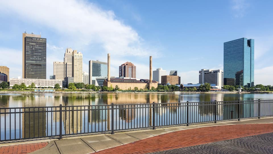 A city skyline with modern buildings and a river in the foreground.