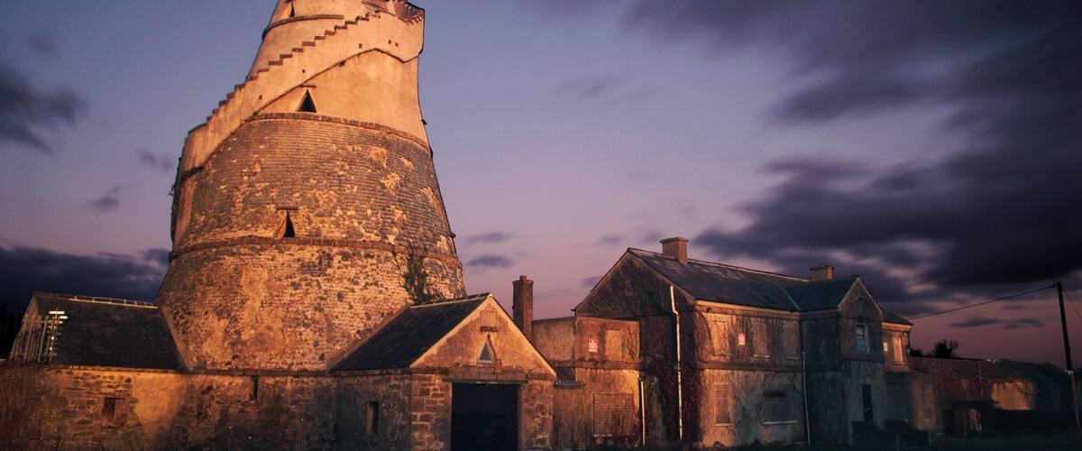 A large stone tower with a conical roof, surrounded by old stone buildings at dusk.