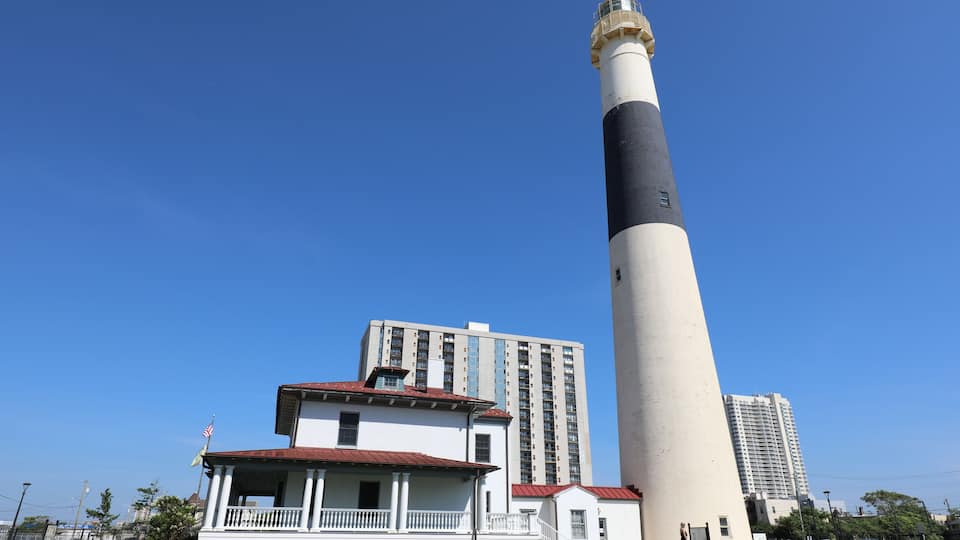 A lighthouse next to a white building with a red roof and a tall tower.