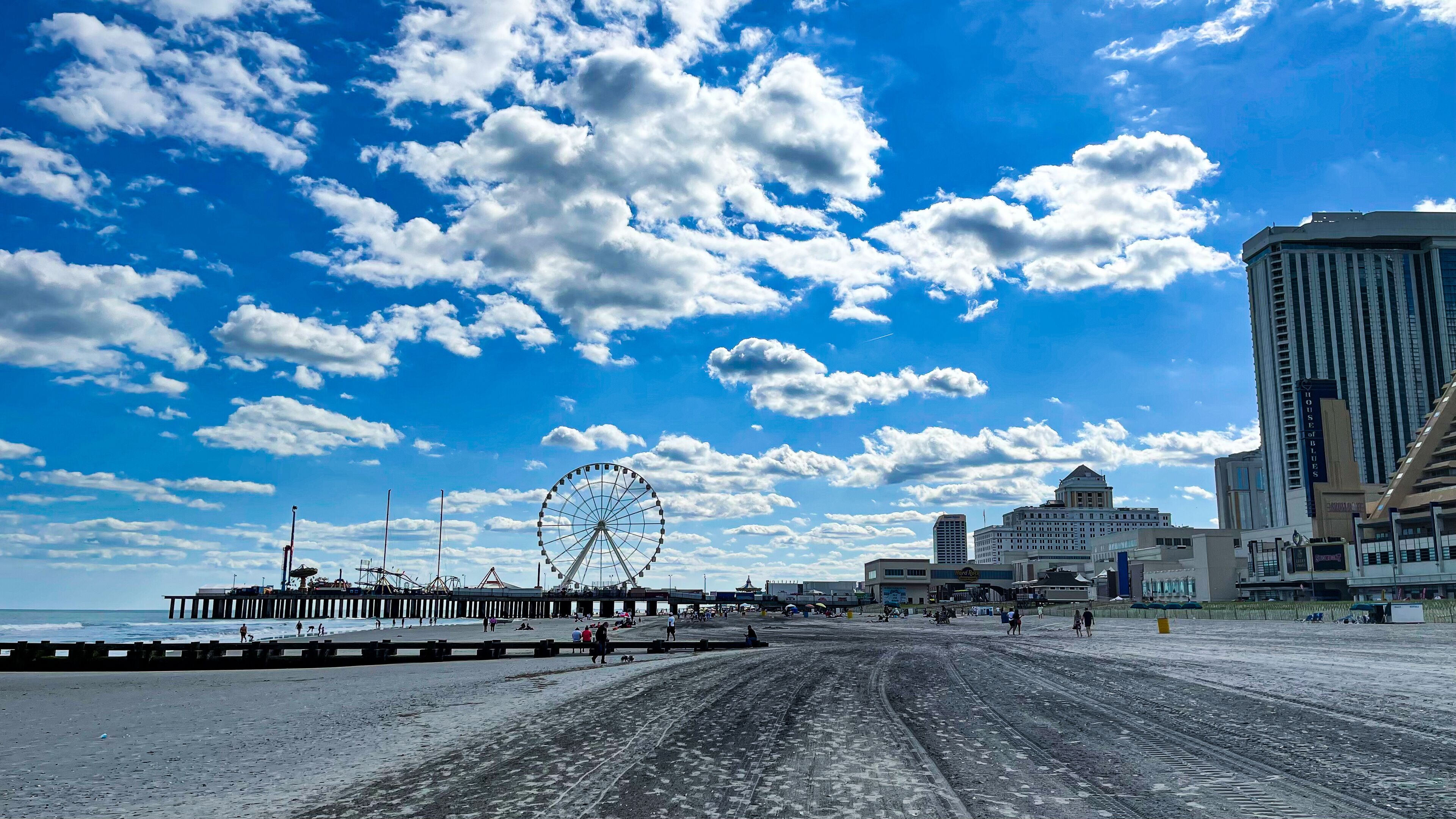 A beach with a Ferris wheel, a pier, and modern buildings in the background.