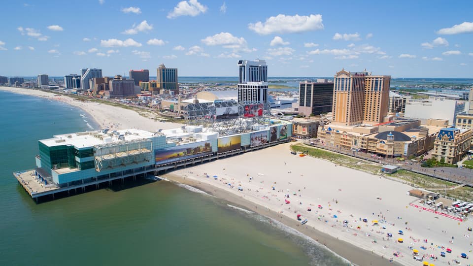 A coastal cityscape with a beach, a boardwalk, and various buildings.