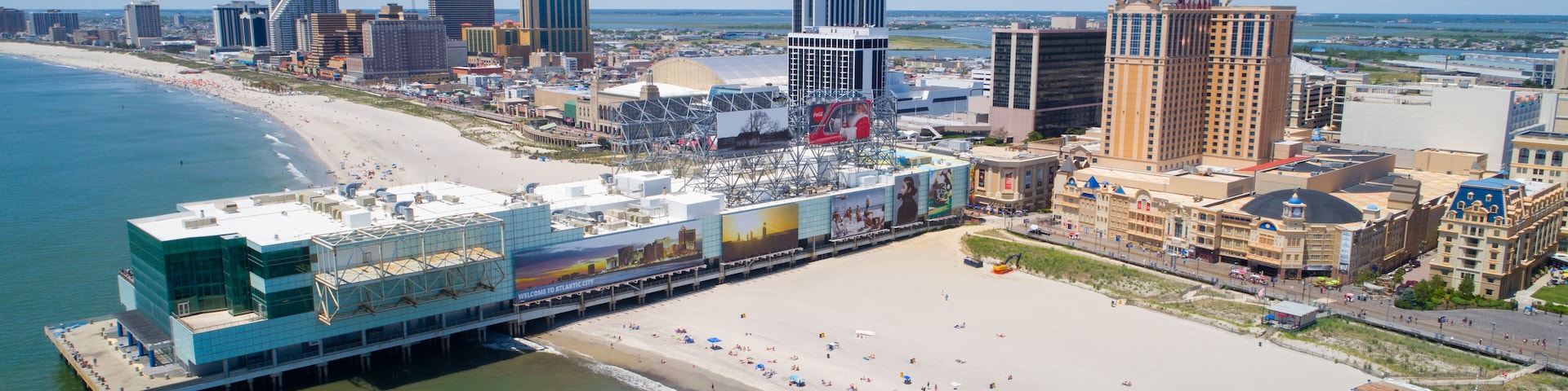 A coastal cityscape with a beach, a boardwalk, and various buildings.