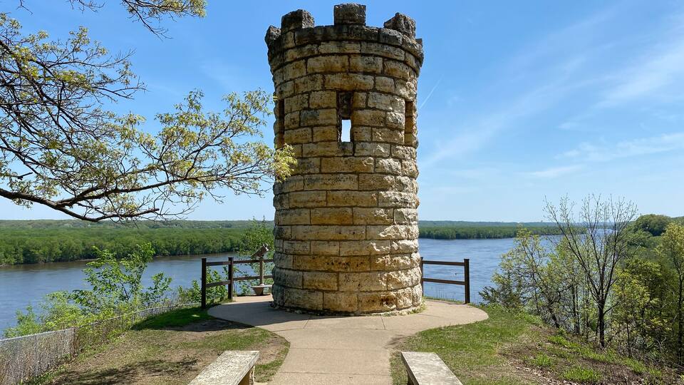 A stone tower by a lake with a path leading to it and benches.