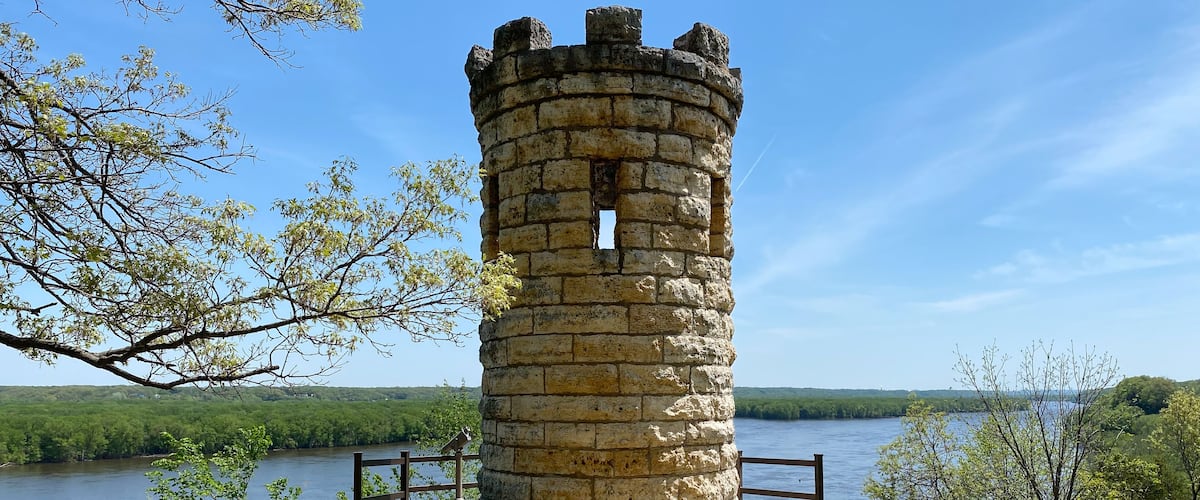 A stone tower by a lake with a path leading to it and benches.