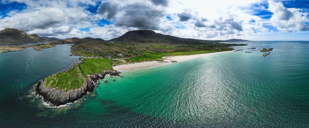 A coastal landscape with a prominent mountain, a sandy beach, and a small island with greenery.