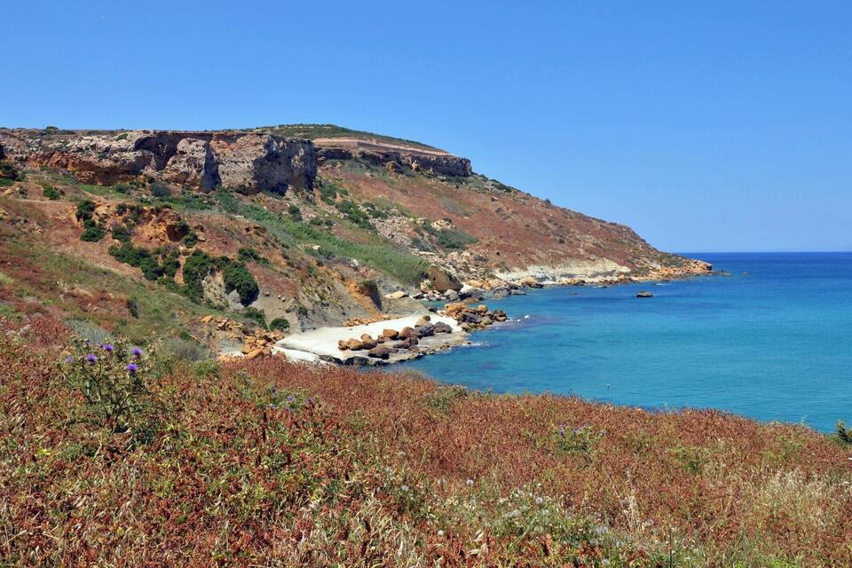 Un paisaje costero con acantilados, una playa y un mar azul y transparente.