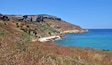 A coastal landscape with cliffs, a beach, and a clear blue sea.