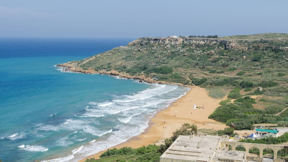 A coastal landscape with a beach, rocky cliffs, and a lighthouse.