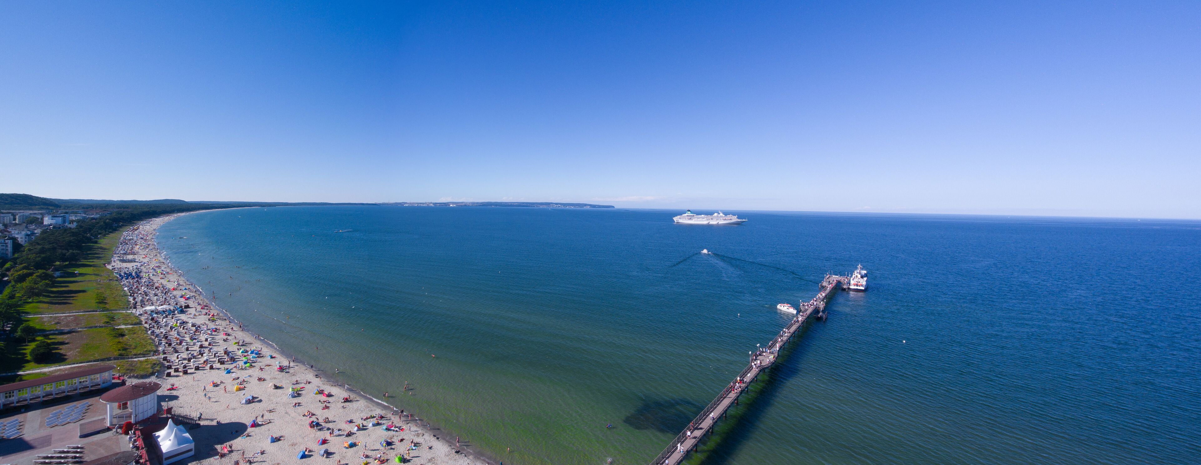 A coastal beach with a pier extending into the sea, a clear sky, and distant landforms.