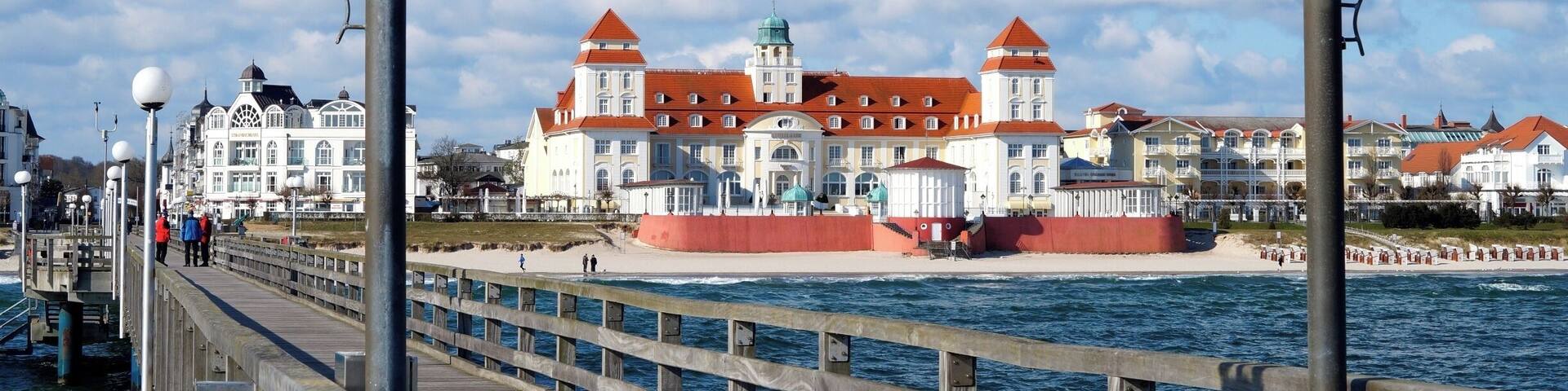 A pier with a sign reading "Seebad Binz" and a large building with red roofs in the background.