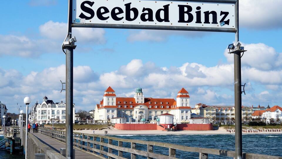 A pier with a sign reading "Seebad Binz" and a large building with red roofs in the background.