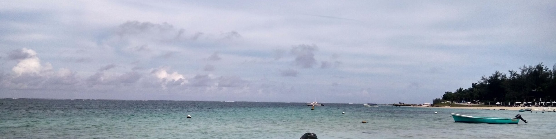A red boat tied to a buoy on a sandy beach with calm waters and a cloudy sky.