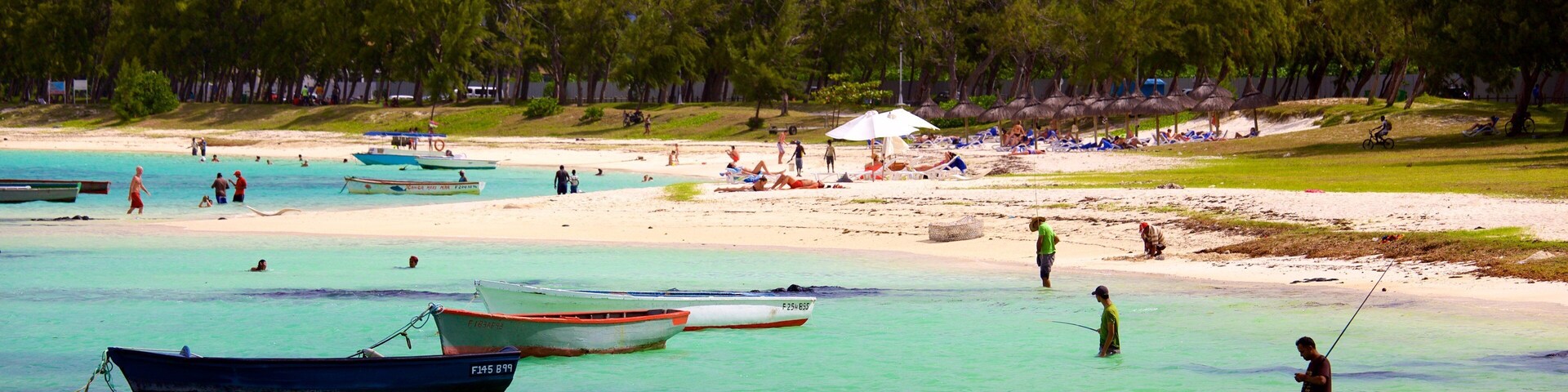 Una playa con barcos, gente pescando y un bosque al fondo.