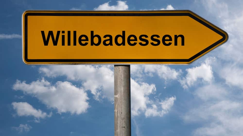 Un panneau de signalisation indiquant la direction de « Willebadesen », avec le texte inscrit sur un fond de ciel bleu parsemé de nuages.