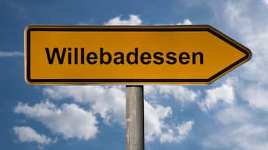 A directional sign with the text "Willebadesen" against a blue sky with clouds.