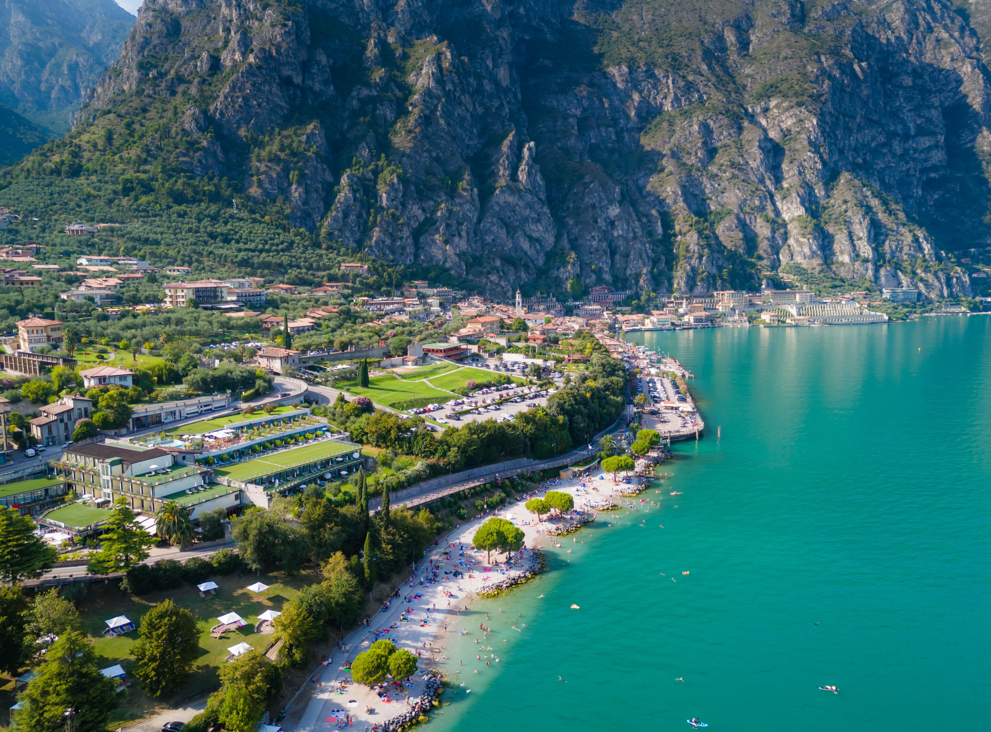 Limone sul Garda beach with people at a beach swimming and sunbathing. Aerial view of panoramic lake Garda. Lombardy drone landscape
