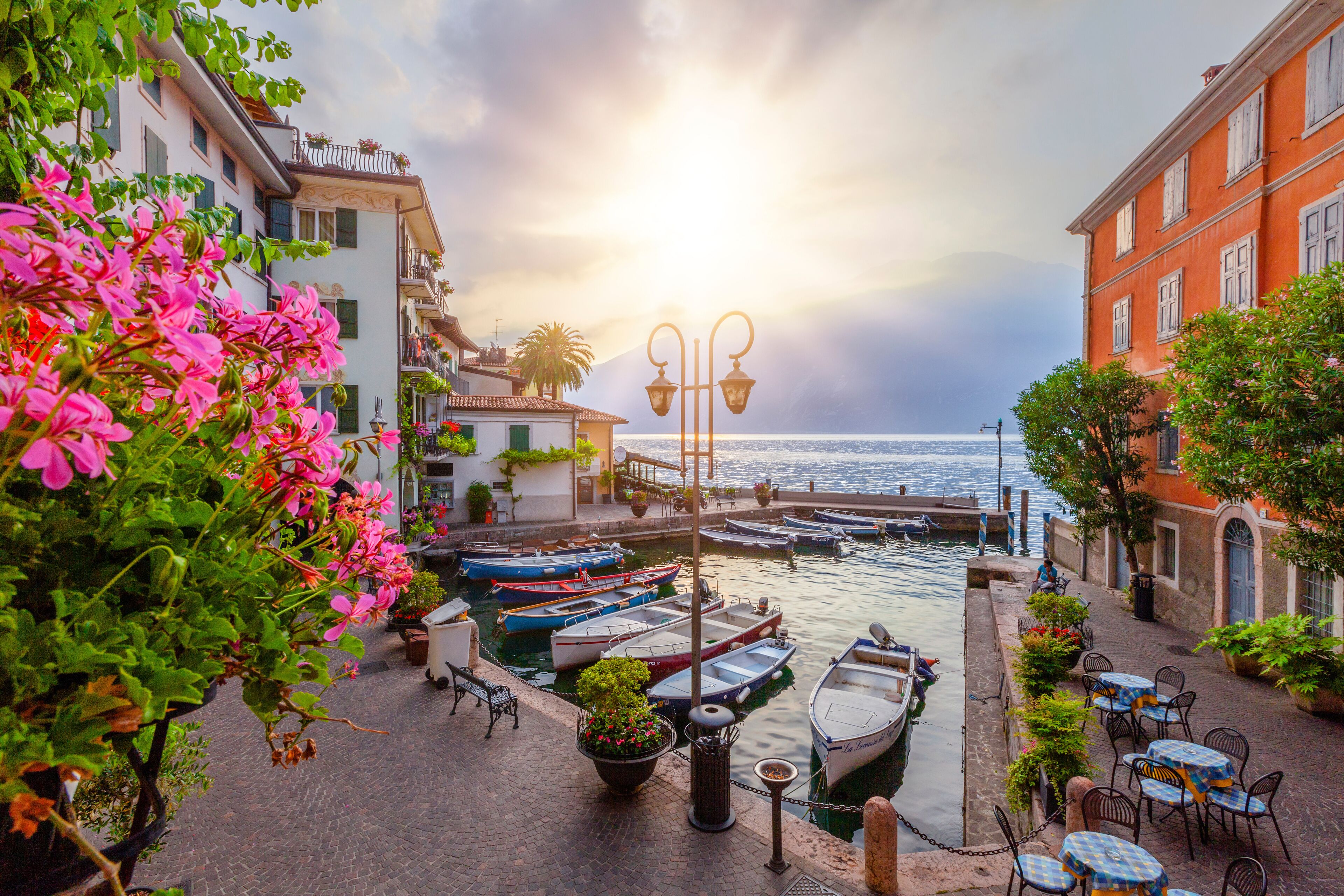 A waterfront with boats docked, a street with cafes, and buildings with balconies.